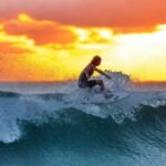 Surfer riding a wave during a stunning sunset, capturing the thrill of water sports.